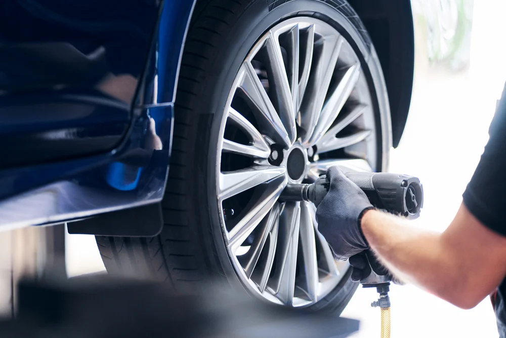 Hand mit Handschuh bedient Schlagschrauber an Felge eines blauen Autos