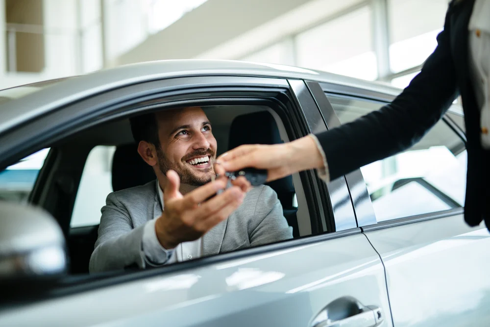 Mann im Auto reicht Schlüssel an stehende Person