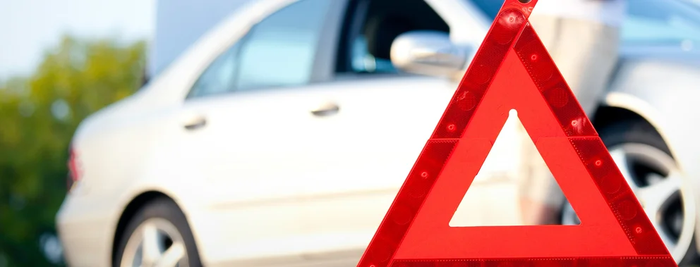 Rotes Warndreieck vor einem weißen Auto auf einer Straße