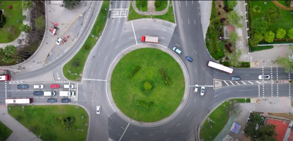 Luftaufnahme eines Kreisverkehrs mit mehreren Fahrzeugen und umliegenden Straßen und Grünflächen
