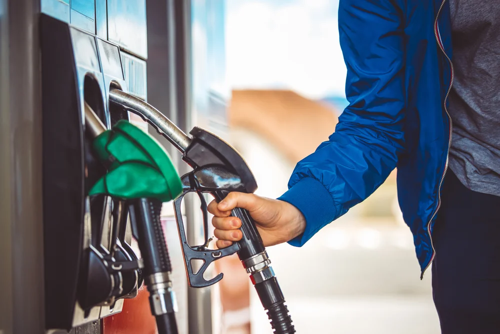 Hand in blauer Jacke hält Zapfpistole an Tankstelle