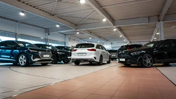 Mehrere Neuwagen verschiedener Marken stehen in einer hell beleuchteten Autohalle auf gefliesten Böden
