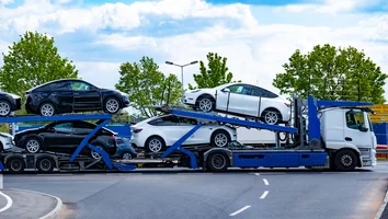 Autotransporter mit mehreren Elektroautos der Marke Tesla auf einer Straße vor Bäumen