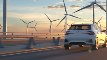 Ein weißes Auto fährt auf einer Brücke mit Windrädern im Hintergrund bei Sonnenuntergang
