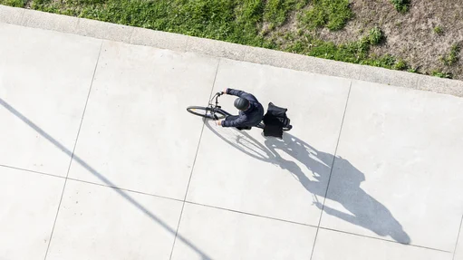 Ein Fahrradfahrer von oben fährt auf einem Gehweg in der Sonne