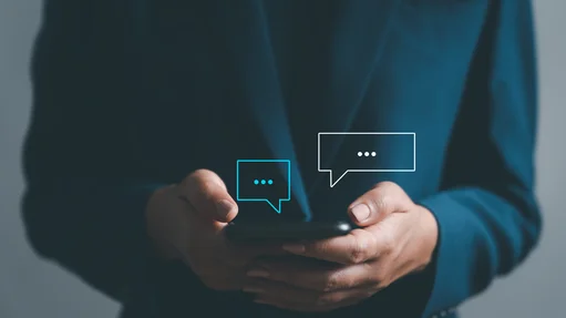 Ein Mann hält ein Handy in der Hand über dem Handy sind zwei Sprechblasen 