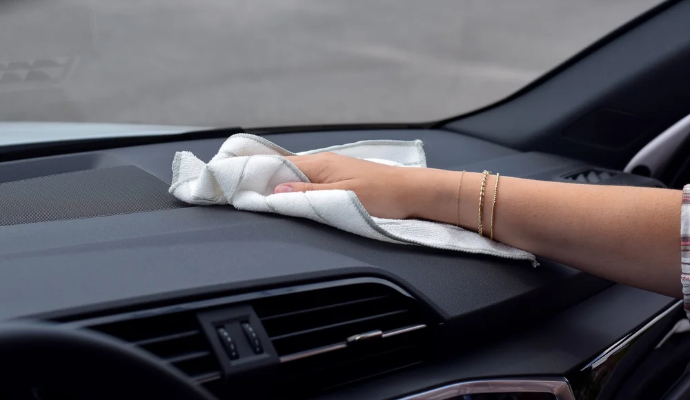 Hand mit Armbändern wischt mit weißem Tuch das Armaturenbrett eines Autos