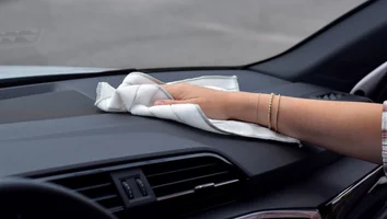 Hand mit Armbändern wischt mit weißem Tuch das Armaturenbrett eines Autos